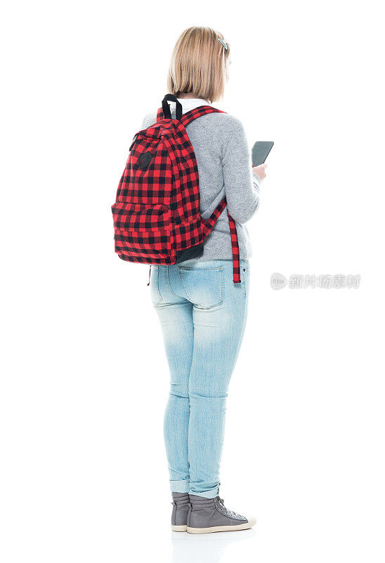 全长/后视图/背面16-17岁美丽的金发z一代年轻女性/少女/学生/高中生/初中生站着学习，拿着手机/包/使用智能手机